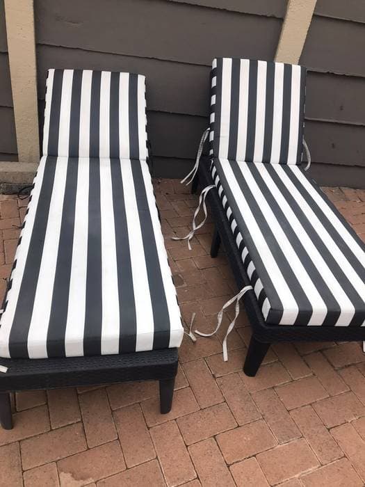 Two black-and-white striped pool lounger cushions, cleaned and set upright on a patio.